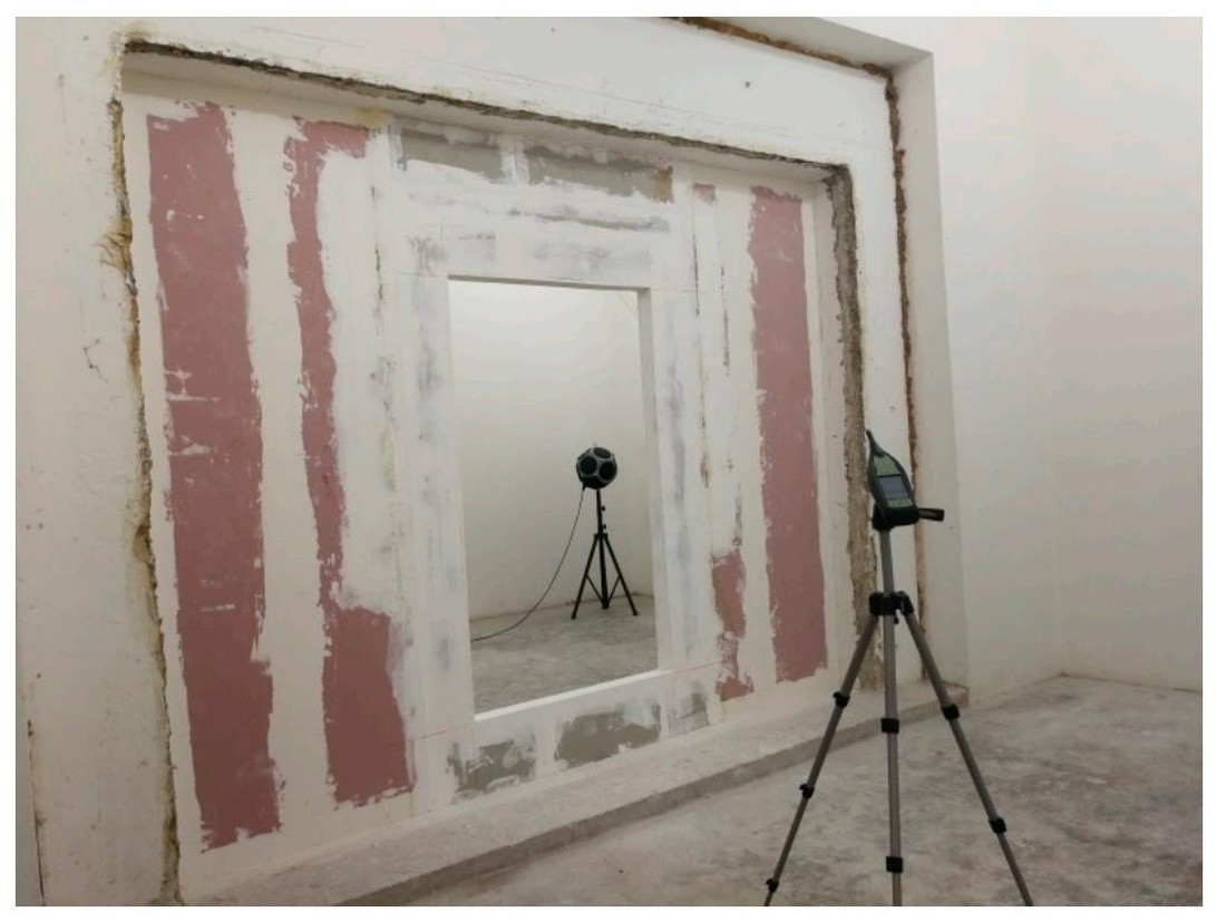 En väggöppning under ljudisoleringsrenovering med synliga rosa isoleringspaneler eller akustikgips.